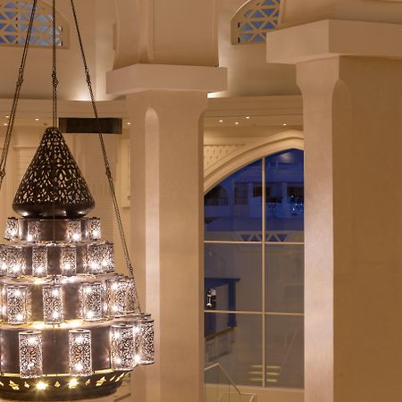 Pickalbatros Palace Sharm - "Aqua Park" Exterior foto The photo shows a beautifully designed chandelier hanging from the ceiling of a spacious interior. The chandelier features a structure with multiple levels and includes ornate patterns, likely made of metal or glass, that diffuse light elegantly. The
