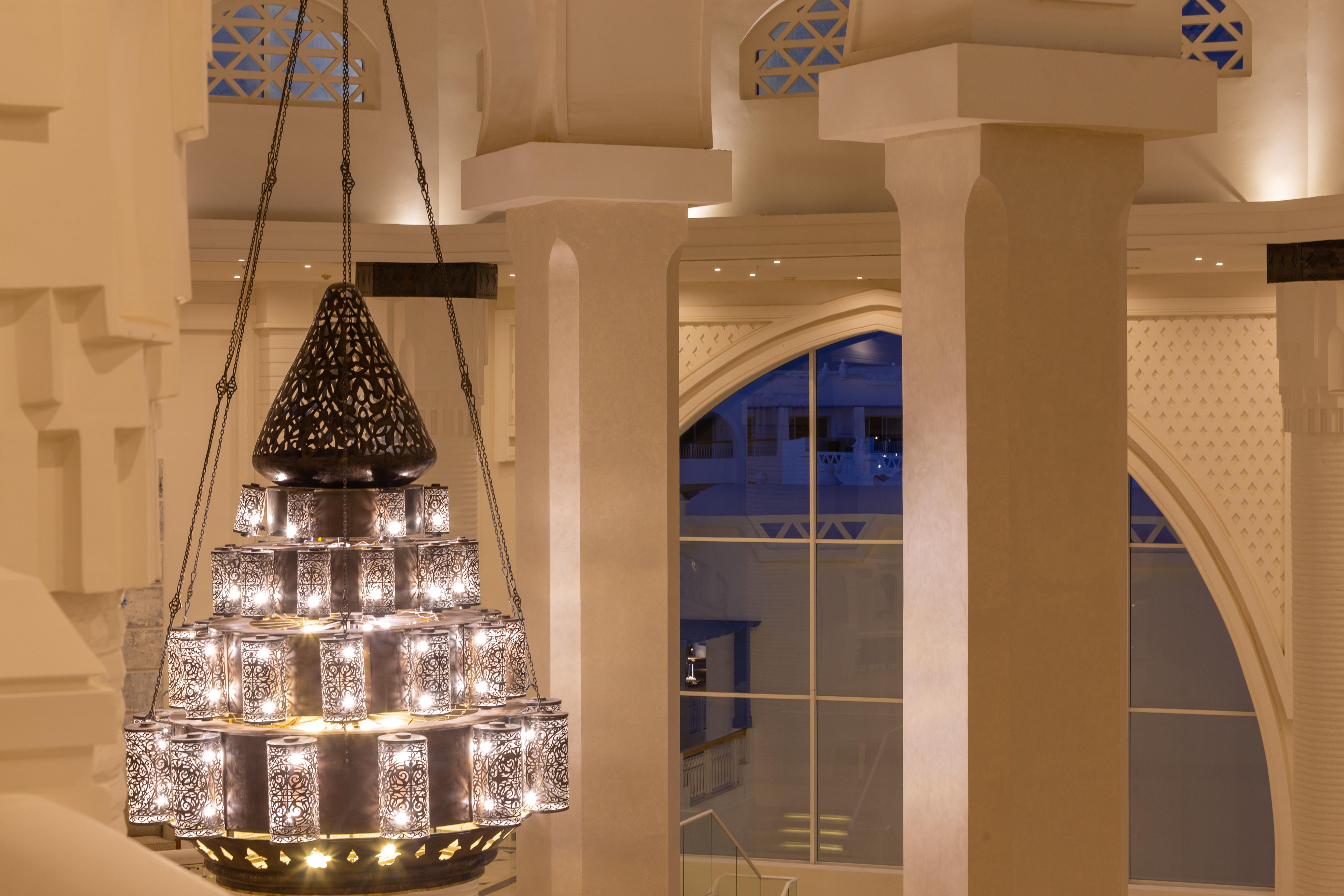 Pickalbatros Palace Sharm - "Aqua Park" Exterior foto The photo shows a beautifully designed chandelier hanging from the ceiling of a spacious interior. The chandelier features a structure with multiple levels and includes ornate patterns, likely made of metal or glass, that diffuse light elegantly. The