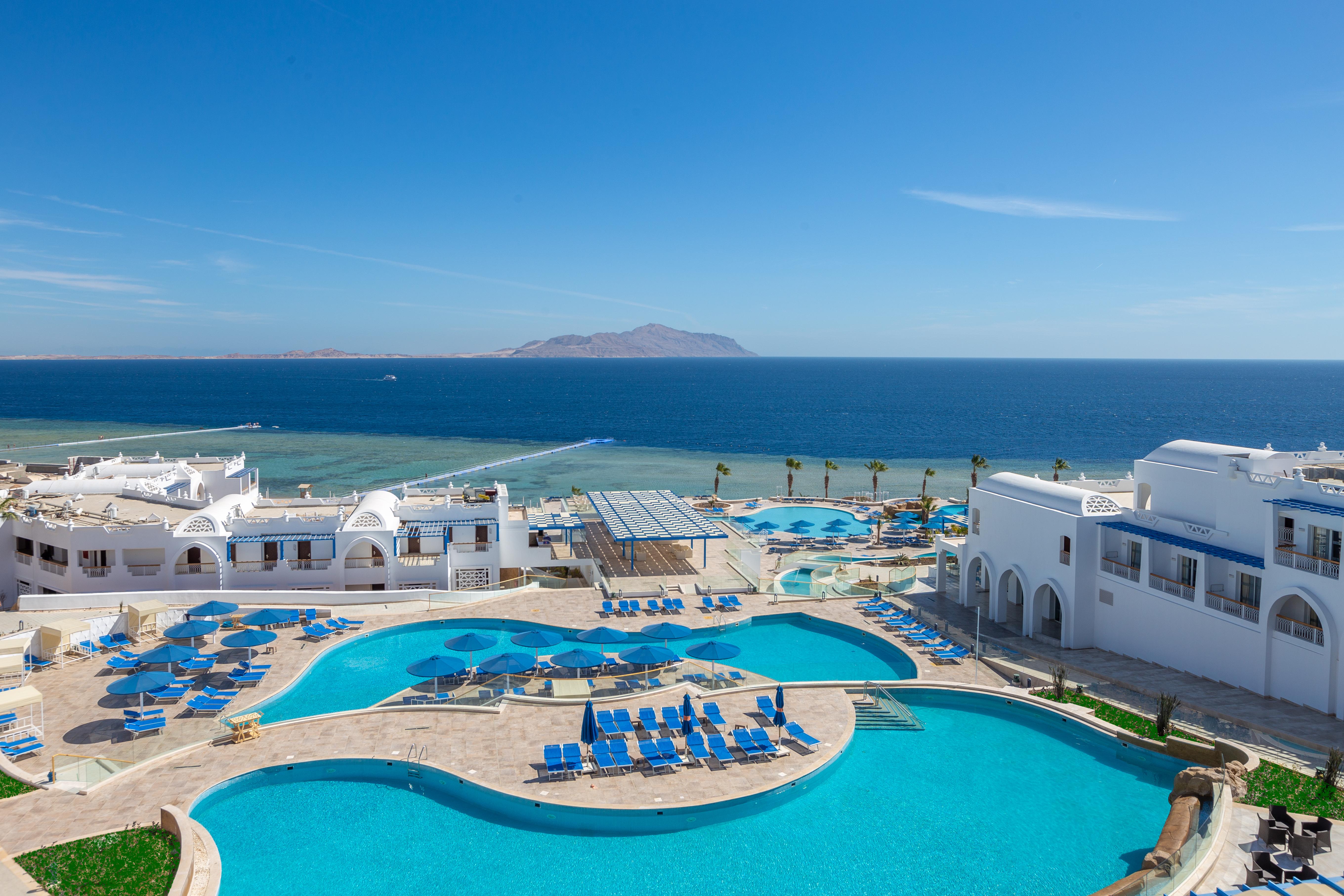 Pickalbatros Palace Sharm - "Aqua Park" Exterior foto The image shows a beautiful seaside resort with multiple swimming pools surrounded by lounge chairs. The pools are designed in various shapes, and the area is adorned with sun umbrellas. In the background, you can see the clear blue ocean and a dista