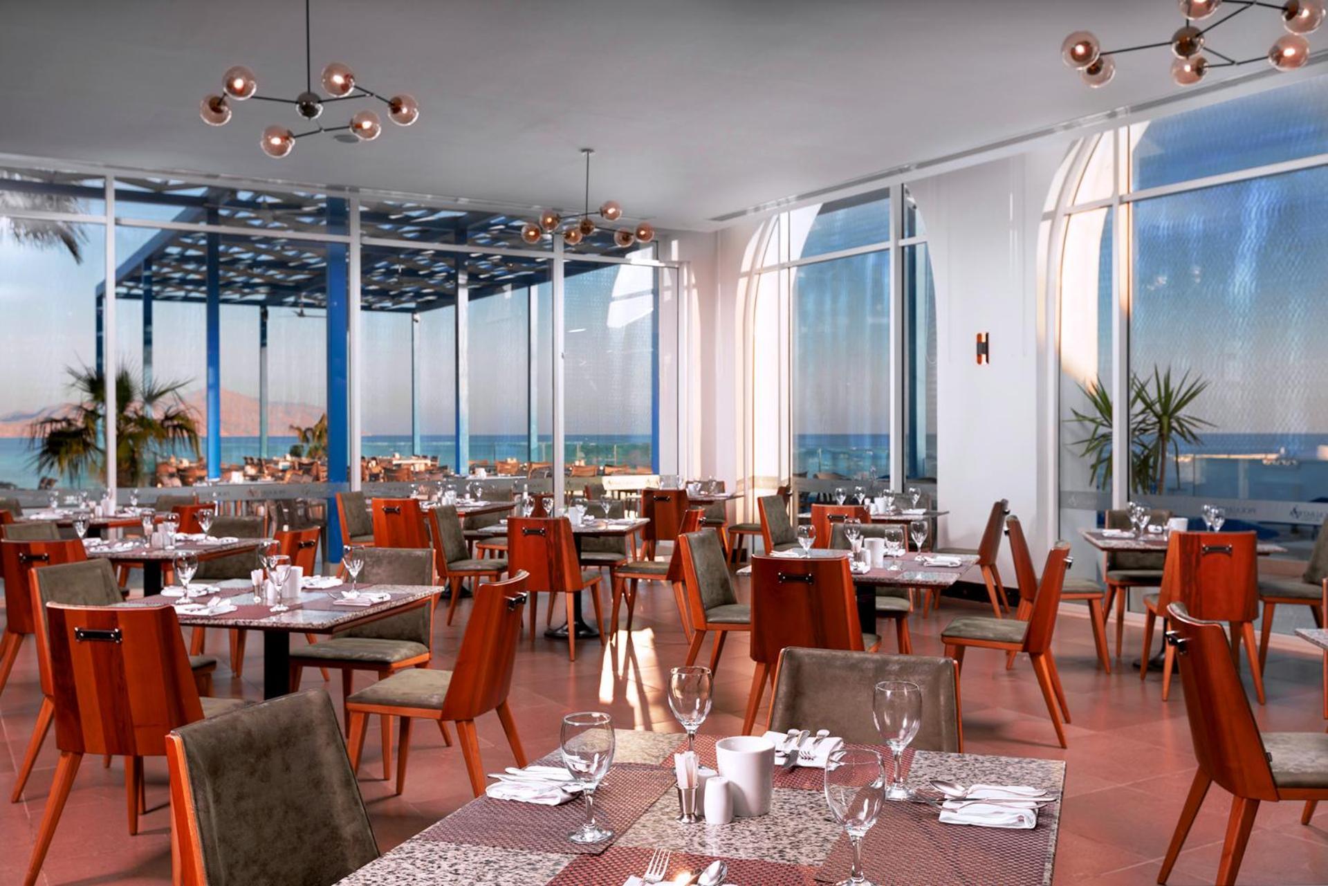 Pickalbatros Palace Sharm - "Aqua Park" Exterior foto The photo shows a modern restaurant interior featuring multiple dining tables arranged neatly across the space. The tables are set with utensils, glasses, and decorations, indicating readiness for guests. Large windows allow plenty of natural light t